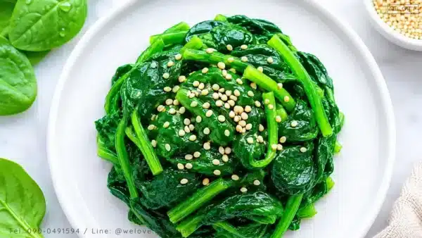 ผักโขมต้มสุกโรยงาบนจานสีขาว ผักใบเขียวที่มีแมกนีเซียมสูง